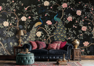 Dark floral peacock wall mural with trailing branches and pink blooms, in a maximalist living room with velvet sofa