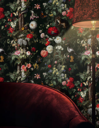 Dark floral wallpaper with roses, birds, and butterflies on black, in a moody lounge with red velvet sofa