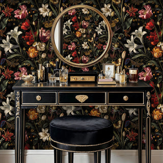 Dark floral wallpaper with vivid botanicals, behind a black vanity table with gold mirror and perfume bottles