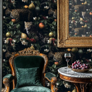 Dark leopard botanical wallpaper with exotic cats and fruits, shown in ornate dining room with green velvet chair