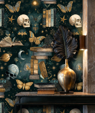 Dark mystical wallpaper with books, skulls and celestial stars in teal and gold, displayed in modern entryway with brass vase