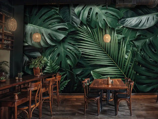 Dark tropical wall mural with monstera leaves and ferns in deep greens, shown in rustic restaurant with wooden tables