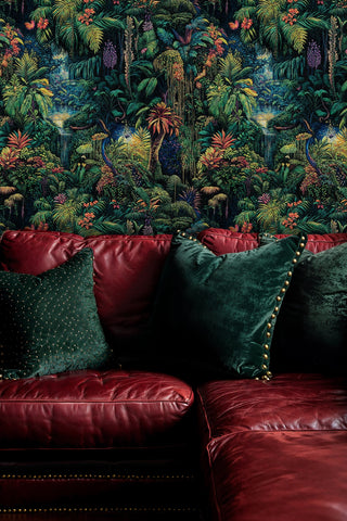 Dark tropical wallpaper with vibrant ferns and exotic flowers, behind a burgundy leather sofa with green cushions