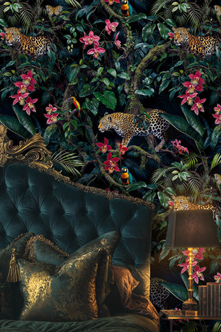 Detailed tropical jungle wallpaper with big cats, lush leaves and pink orchids on dark, shown with a tufted velvet headboard and brass lamp