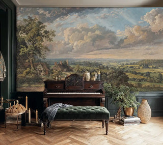 Detailed view of a pastoral landscape wall mural with cottages, fields and luminous clouds in green and blue, classic painted style, shown behind an upright piano and tufted bench