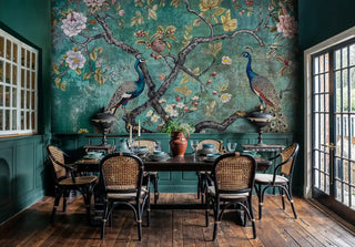 Detailed view of a peacock chinoiserie wall mural in teal and gold, with rattan chairs