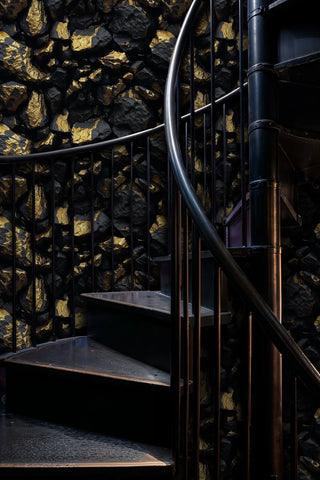 Dramatic black and gold stone wallpaper creating bold statement wall on elegant curved staircase