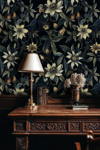 Dramatic botanical clematis wallpaper in dark tones, styled in study room with brass table lamp and books