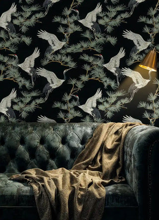 Dramatic crane wallpaper with pine grove design, displayed in luxurious living room with tufted velvet sofa and golden throw blanket