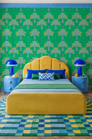 Embroidered palm tree wallpaper in green and yellow displayed in a bold bedroom with scalloped headboard