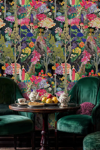 Enchanted garden wallpaper with vibrant florals and whimsical figures, shown in elegant dining room with emerald chairs