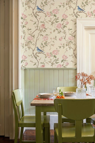 English garden wallpaper featuring pink roses and blue birds on branches, shown in cozy dining room with green chairs