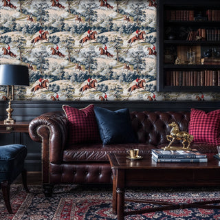 Equestrian scenic wallpaper with horses, riders and wooded landscape, blue and beige tones, in a dark study with chesterfield sofa