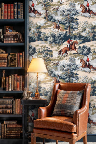 Equestrian scenic wallpaper with riders, horses and trees, blue and beige tones, in a library with leather chair