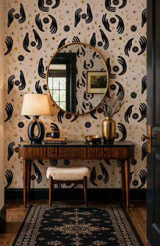 Evil eye and celestial hands wallpaper in beige and black in an entryway with round gold mirror and console table