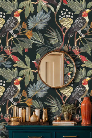 Exotic bird wallpaper with toucans and tropical foliage shown in powder room with round copper mirror and brass accessories