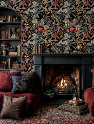 Exotic leopard jungle wallpaper with spotted cats and coral flowers on black, shown in cozy study with fireplace