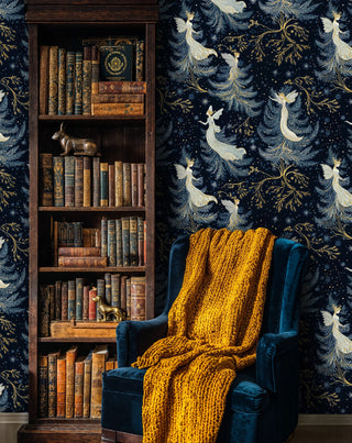 Fairy wallpaper with flowing gowns, stars and gold branches in navy, styled beside a bookcase and blue chair