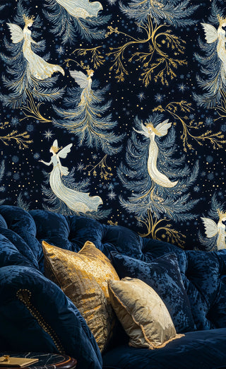 Fairy wallpaper with white winged figures and glittering branches in navy, behind a tufted blue sofa with gold pillows