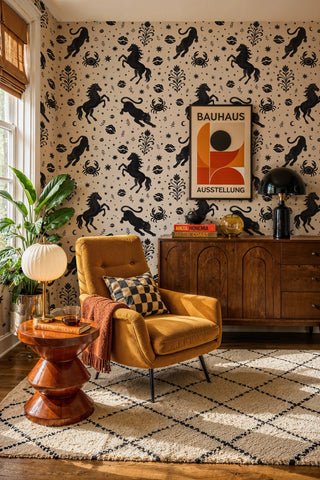 Folk art wallpaper with rearing horses and crabs in black on cream, in a living room with mustard armchair