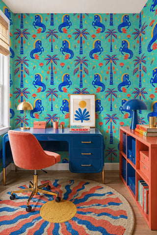 Folk-style horse and palm wallpaper on turquoise ground in a home office with blue desk and coral chair