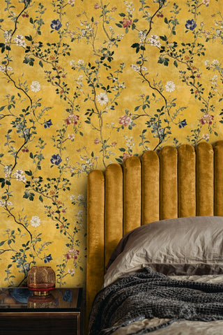 Gold floral chinoiserie wallpaper with delicate blossoms and vines, behind a mustard velvet channel headboard and amber vase