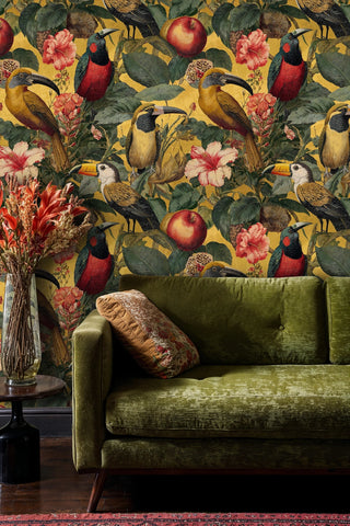 Gold tropical bird wallpaper with toucans and lush leaves, in a living room with green velvet sofa