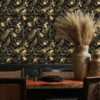 Golden botanical wallpaper with ferns and wildflowers on black, shown in rustic dining space with ceramic vases
