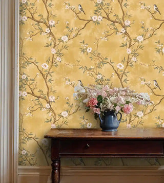 Golden chinoiserie bird wallpaper featuring delicate branches and blooms, displayed in traditional dining room with antique table
