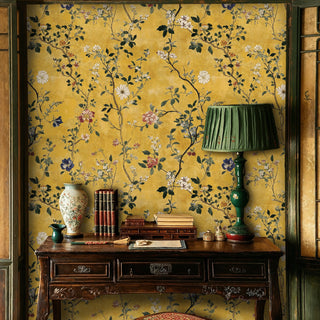 Golden chinoiserie wallpaper with flowering branches and lush leaves, shown in a study with antique desk and green lamp