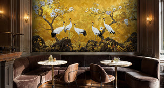 Golden floral crane wall mural with dark foliage, in a moody lounge with velvet banquette and wall sconces