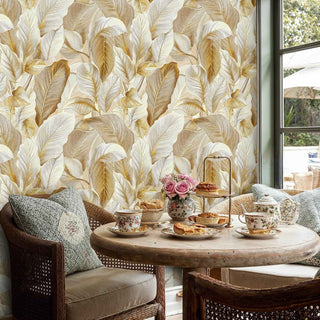 Golden tropical leaf design wallpaper, shown in bright sunroom with wicker furniture and tea service