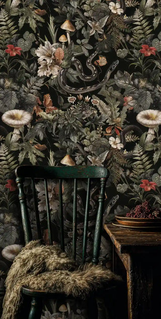 Gothic botanical wallpaper displaying snakes and flowers in rustic setting with antique green chair and fur throw