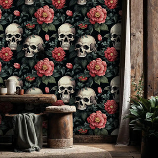 Gothic botanical wallpaper with skulls and coral flowers, displayed in rustic setting with wooden stools
