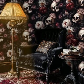 Gothic skull and floral wallpaper in a moody study featuring a black velvet armchair and a vintage pleated floor lamp.
