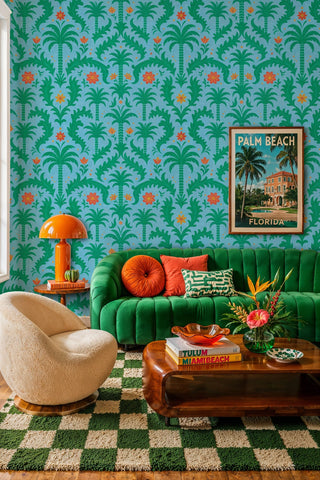 Green palm damask wallpaper with orange blooms on blue, in a living room with green velvet channel sofa