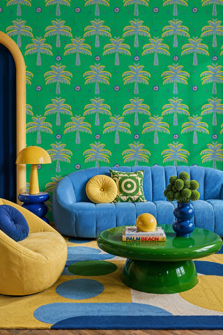 Green palm tree wallpaper with blue and yellow embroidered palms in a colorful living room with blue sofa