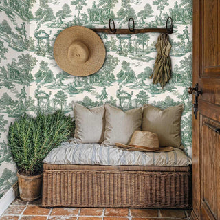 Green toile wallpaper with pastoral scenes and ornate details, displayed in rustic entryway with wicker bench