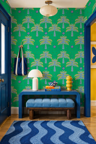 Green tropical palm pattern wallpaper with blue accents in a colorful entryway with wave-print rug