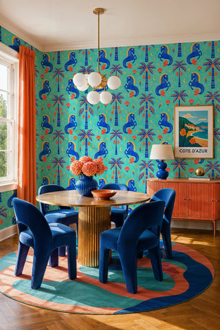 Horse and palm tree pattern wallpaper in a dining room with gold pedestal table and blue velvet chairs