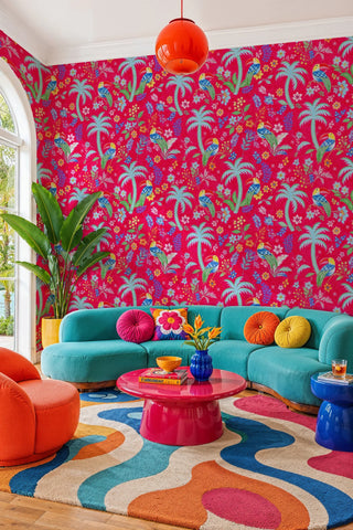 Hot pink toucan wallpaper with palms and wildflowers, in a maximalist living room with teal curved sofa
