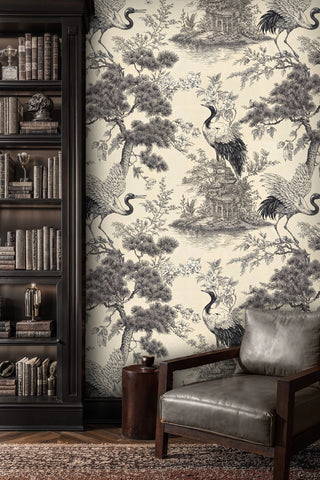 Japanese crane scenic wallpaper in black and cream with garden pavilion, beside a dark bookcase and armchair