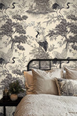 Japanese crane toile wallpaper with pine trees and pavilions in black on cream, in a bedroom with iron bed