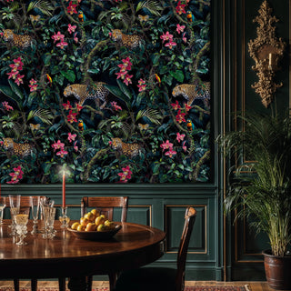 Jungle wallpaper with big cats, lush leaves and pink orchids on dark, shown in a dining room with round table and red taper candle