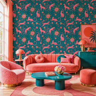 Leopard and sun celestial wallpaper in pink on teal, in a maximalist living room with coral sofa and teal coffee table