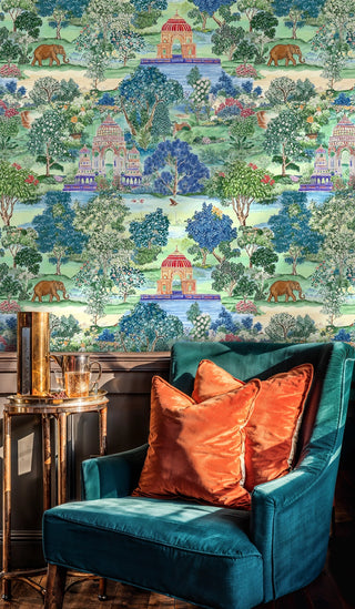 Lush Indian garden wallpaper featuring domed pavilions and elephants in teal and green, with a velvet armchair and orange pillows