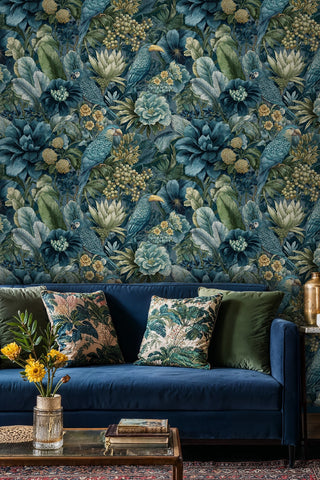 Lush jungle wallpaper with teal parrots and golden flowers shown behind a navy velvet sofa with botanical cushions