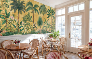 Lush tropical wall mural with detailed flora and hidden birds, displayed in charming cafe setting with French doors and rattan bistro chairs