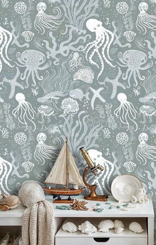 Marine wallpaper featuring octopi and coral in sage green, shown in coastal bedroom with nautical telescope