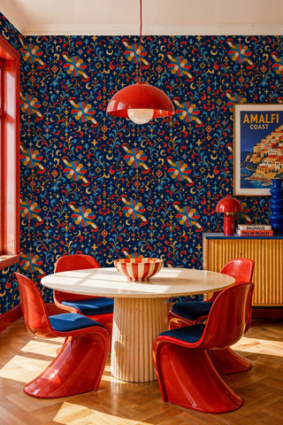 Medieval angel wallpaper with ornate scrollwork in navy, red, and gold, in a dining room with red chairs